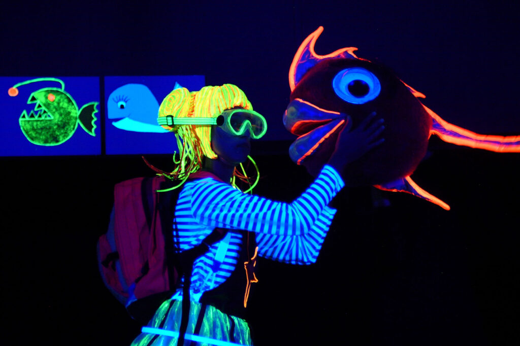 Escena de luz negra con accesorios fluorescentes del tema marino para despertar la curiosidad de los niños.